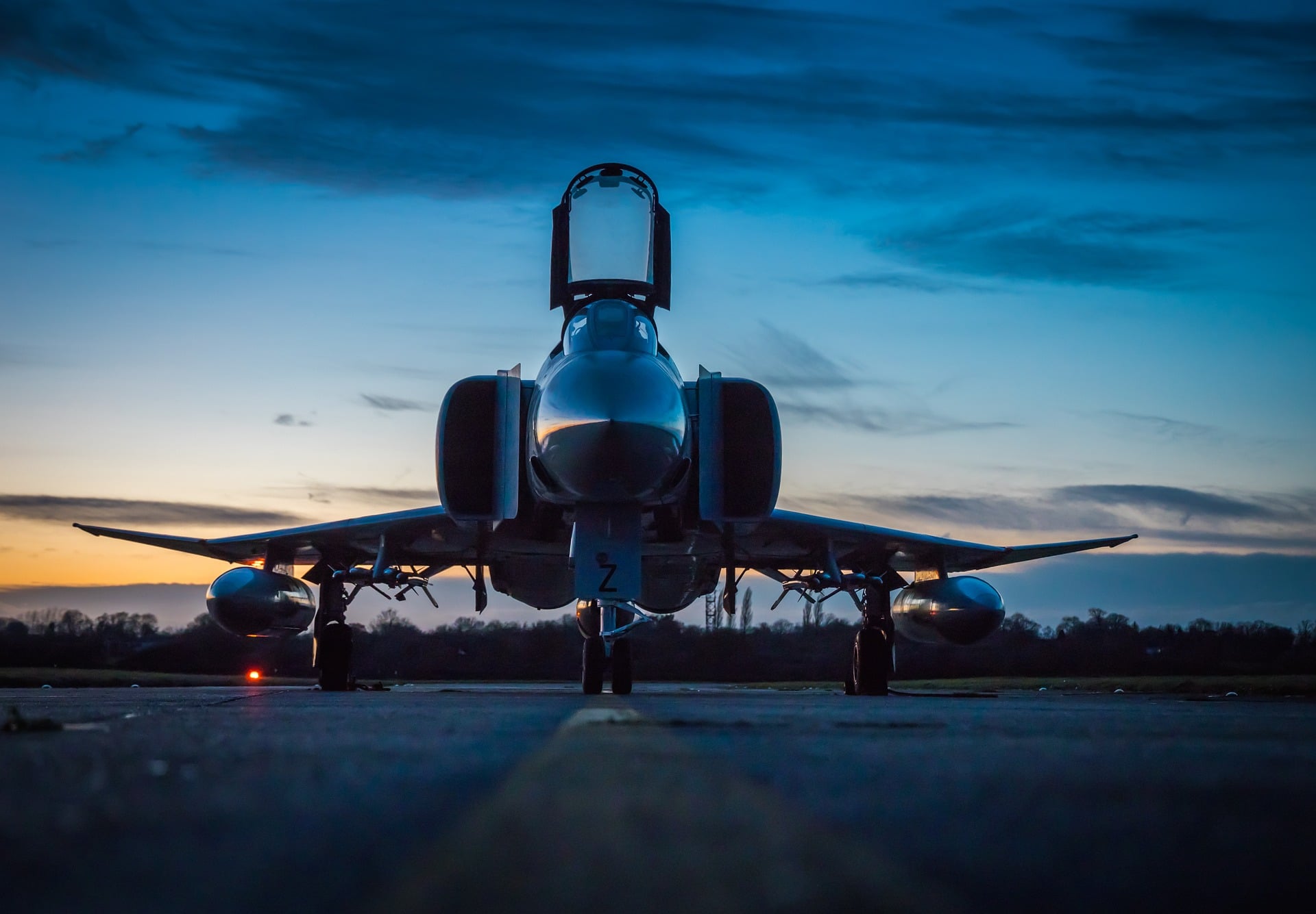 A sleek fighter jet on a runway at dusk under a blue and orange sky.