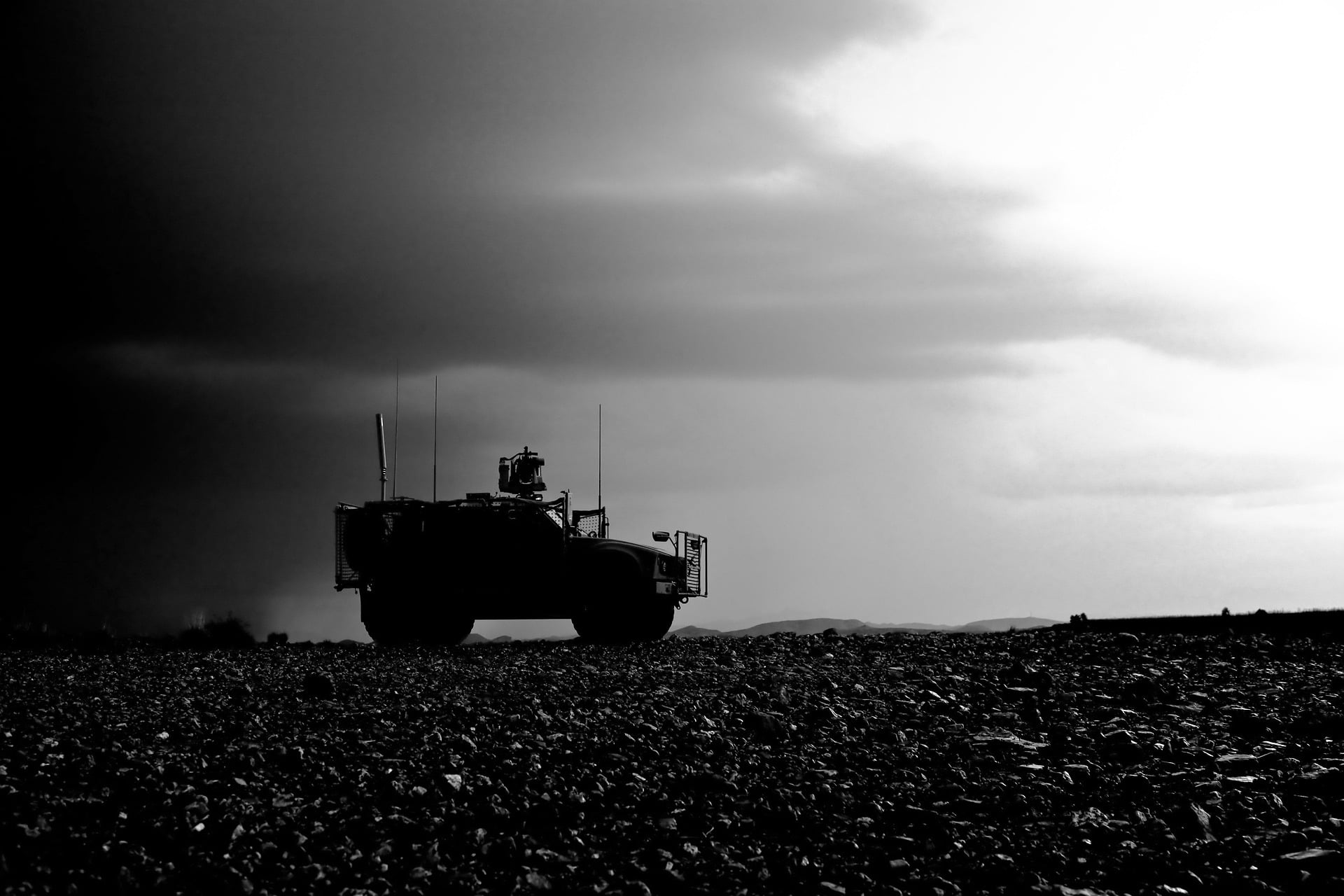 Silhouette of an armored military vehicle on flat, rocky ground under a cloudy sky.