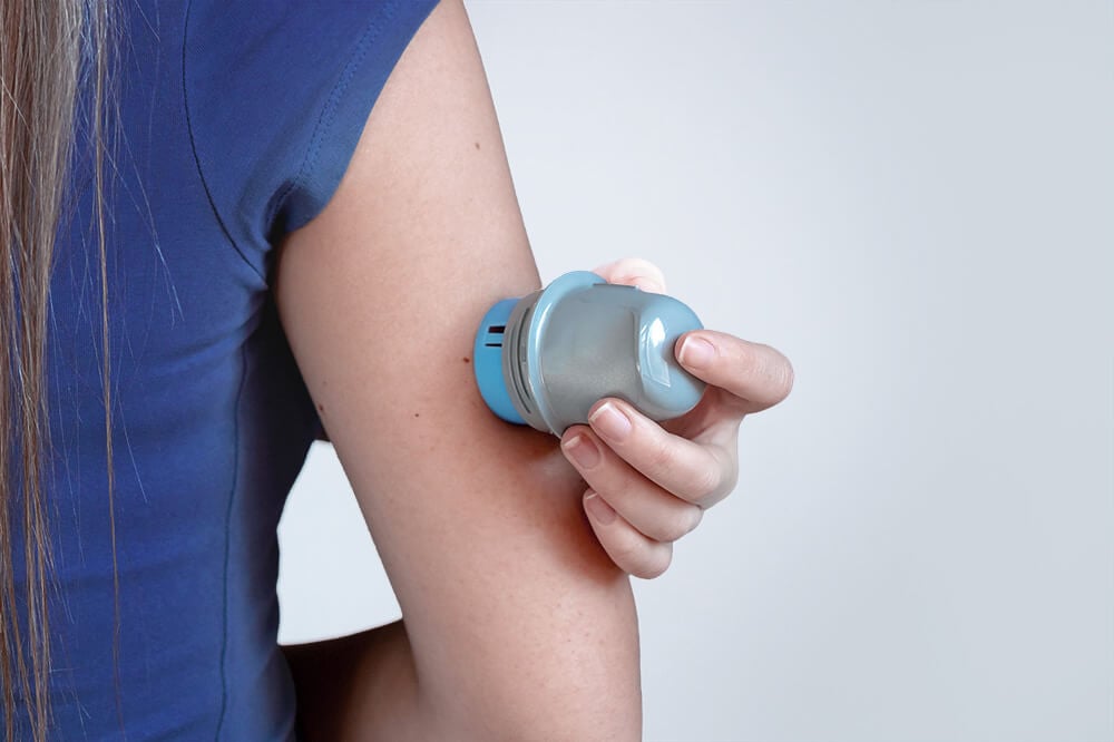 A person in a blue shirt applies a continuous glucose monitor to their upper arm with a handheld device.